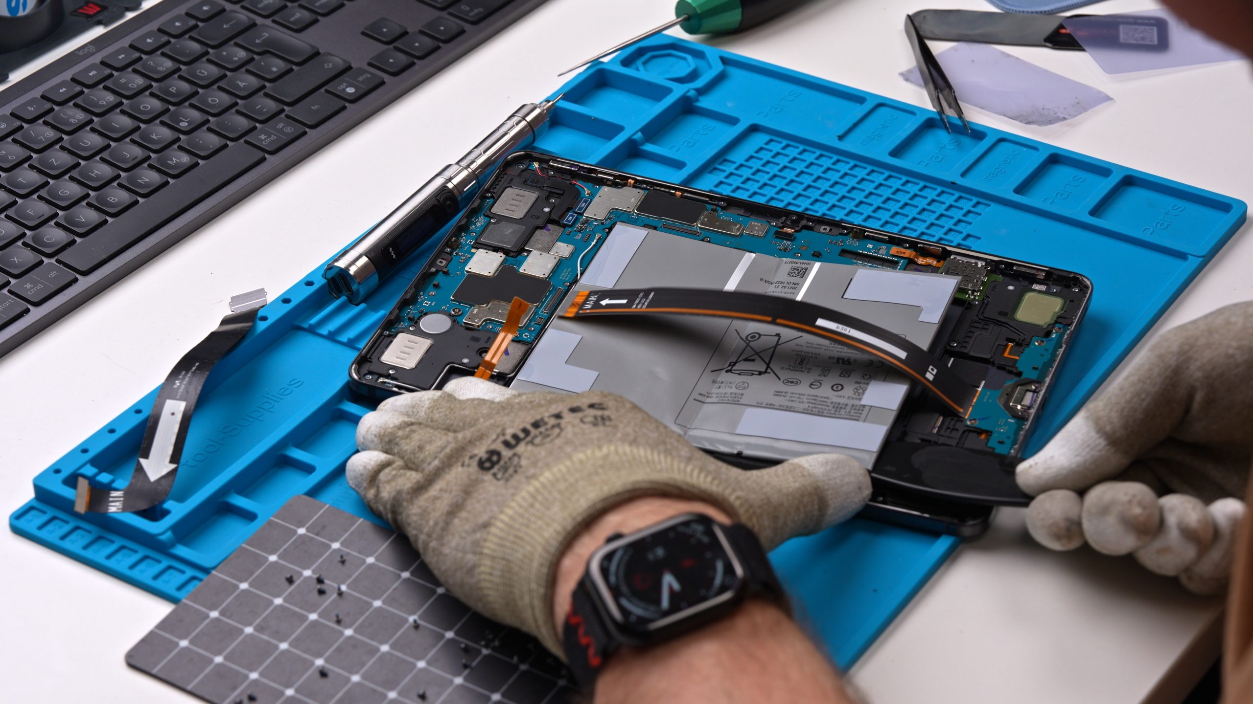 Ein geöffnetes Samsung Tablet liegt auf einer blauen Werkstattmatte; der Akku ist sichtlich aufgebläht und wird von einem Techniker fachgerecht für den Austausch vorbereitet.